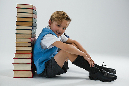 Portrait of schoolboy sitting against books stack on white background