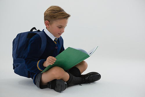 Adorable schoolboy reading book while sitting on white background
