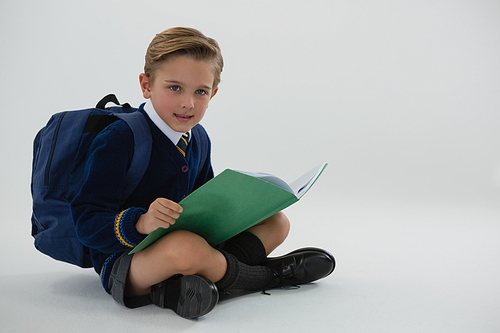 Portrait of schoolboy reading book while sitting on white background