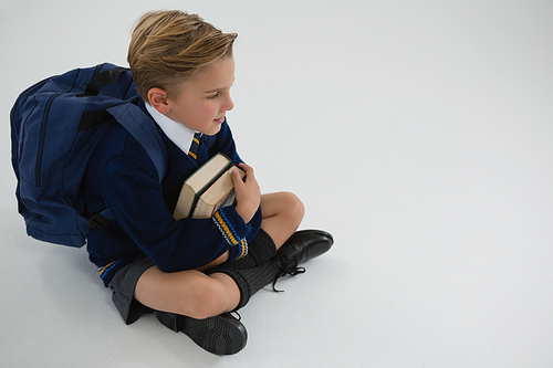 Thoughtful schoolboy sitting with books on white background