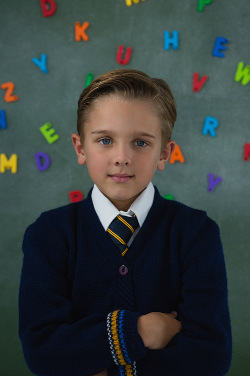 Portrait of schoolboy standing with arms crossed against chalkboard