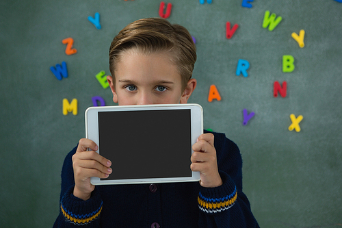 Portrait of schoolboy holding digital tablet against chalkboard