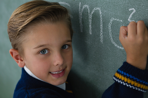 Portrait of schoolboy writing maths formula on chalkboard