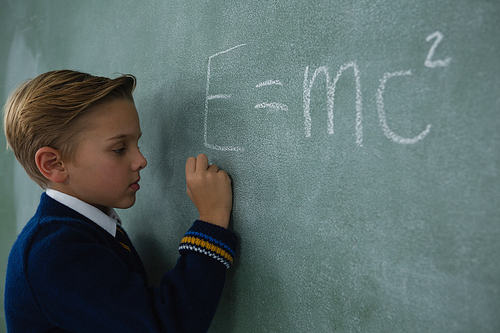 Adorable schoolboy writing maths formula on chalkboard