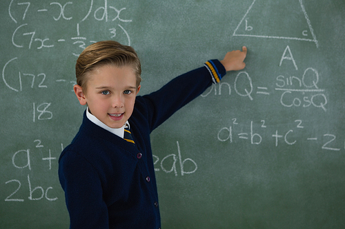 Portrait of schoolboy solving maths formula on chalkboard