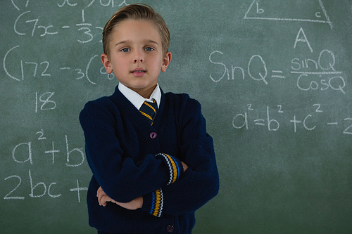 Portrait of schoolboy standing arms crossed against chalkboard