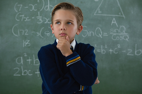 Thoughtful schoolboy standing against chalkboard