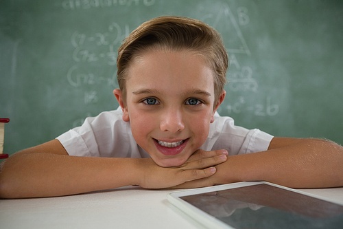 Portrait of schoolboy relaxing on table in classroom