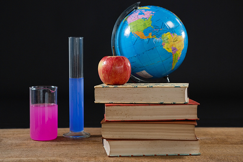 Close-up of globe and books stack with apple on top against black background