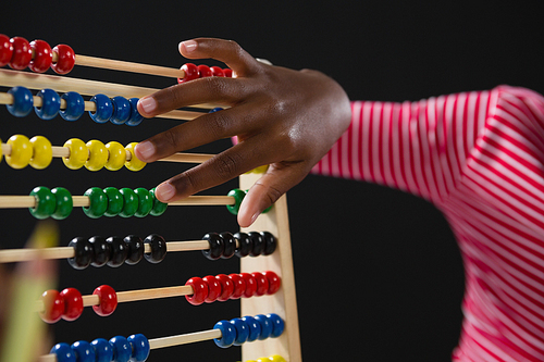 Mid-section of schoolgirl using abacus against black background
