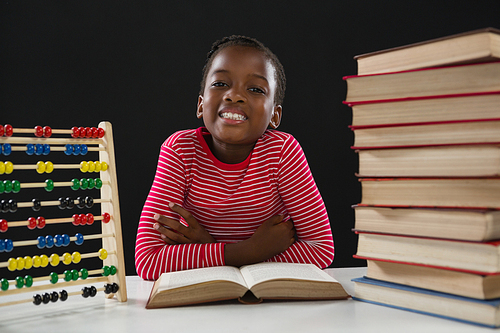 Cute girl with abacus and stack of books against black background