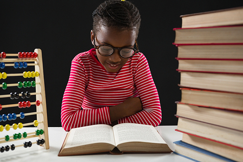 Smiling schoolgirl reading book against black background