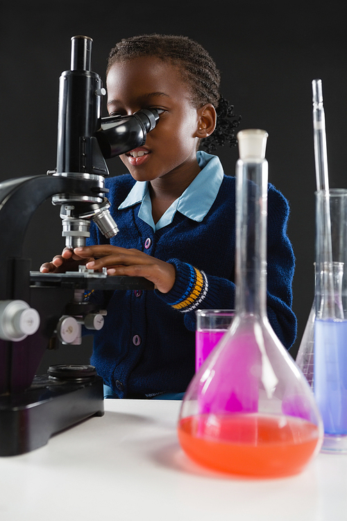 Attentive schoolgirl using microscope against black background
