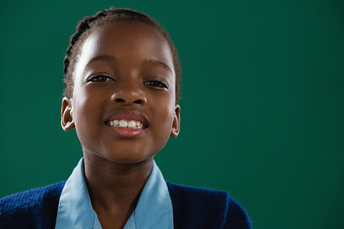 Portrait of smiling schoolgirl standing against green background