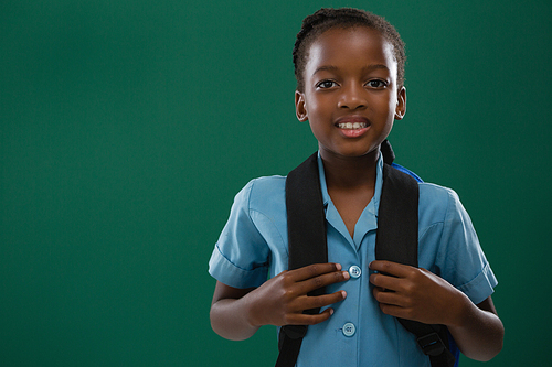 Smiling school girl with backpack standing against chalk board