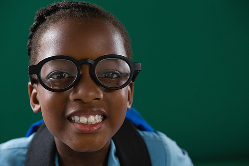 Portrait of smiling schoolgirl with spectacles standing against green background