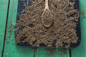 Close-up of cumin with spoon in tray on wooden table