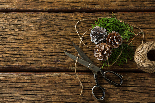 Overhead view of pine cones with scissor and thread spool on wooden table