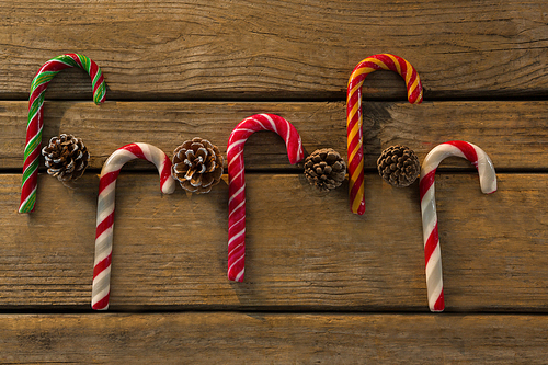 Directly above shot of colorful candy canes with pine cones on wooden table