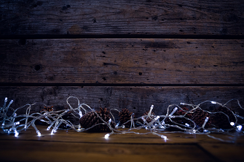 Christmas light and pine cones on wooden plank during christmas