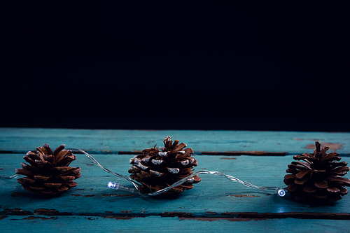 Pine cone decorated with christmas light on wooden plank