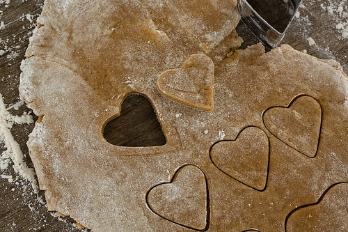 Raw cookie dough with heart shaped cookie cutter on wooden table