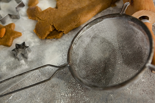 Close-up of stainer and cookie dough with flour on table