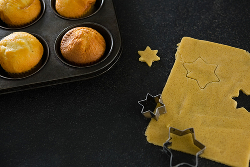 Plain cupcakes in baking tray with star shape dough and cutter on table