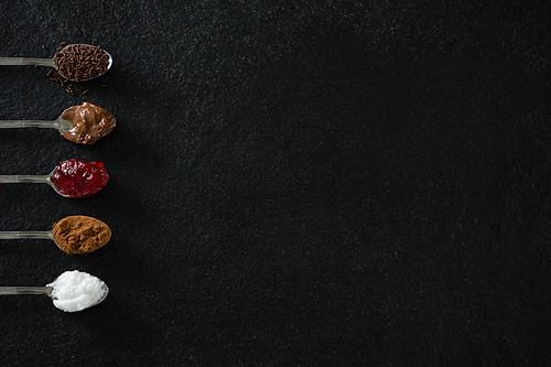 Various cookies seasoning ingredients in spoon on black background