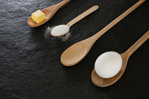 Wooden spoons with egg, cheese cube and powdered sugar on black background