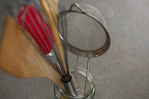 Close-up of whisker, wooden spoon, strainer and spatula on jar