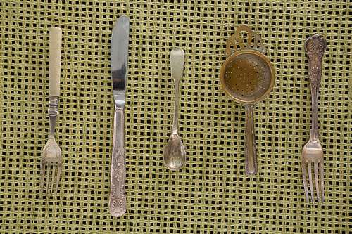 Close-up of spoons, fork, butter knife and strainer on place mat