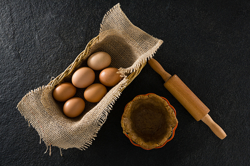 Eggs in wicker basket with dough on table