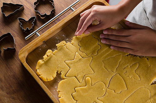 Mid-section of man removing gingerbread dough on wooden table