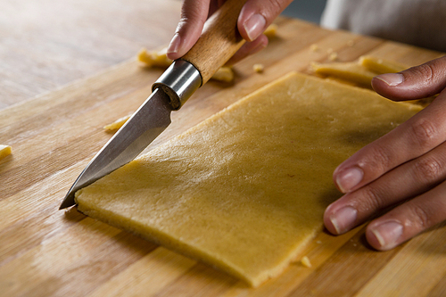 Close-up of woman slicing dough on chopping board