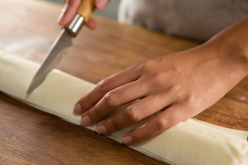 Close-up of woman slicing dough on chopping board
