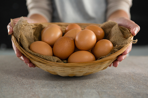 Mid-section of woman holding basket with brown eggs