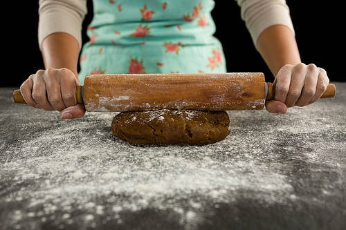 Mid-section of woman baking dough with rolling pin