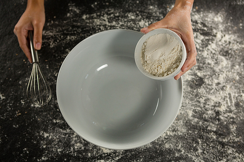Close-up of woman holding whisk and bowl with flour
