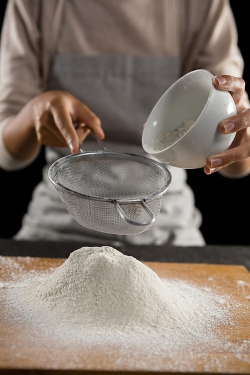 Mid section of woman sieving flour from the bowl on the wooden board