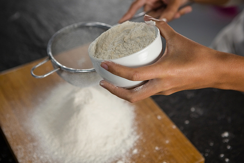 Close-up of woman sieving flour from the bowl on the wooden board