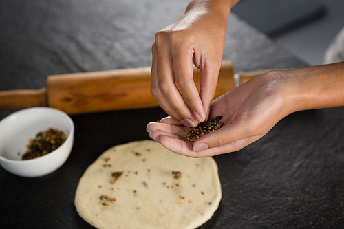 Close-up of woman adding dry fruits over flattened dough