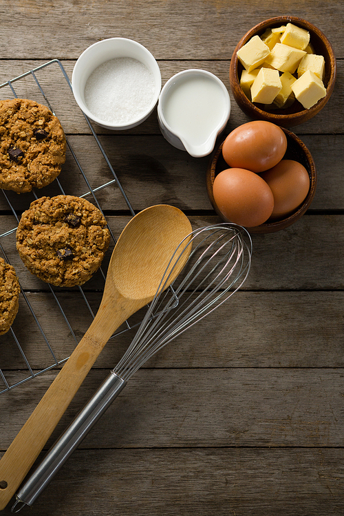 Over head view of fresh baked cookies, whisk, eggs, flour on wooden table