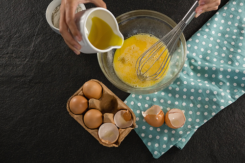 Over head view of woman adding oil into beaten eggs in a bowl