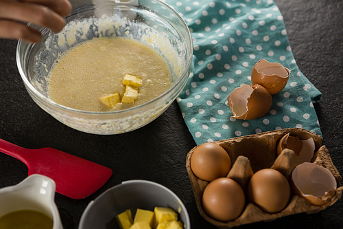 Woman adding butter cube to batter of beaten eggs and milk in a bowl