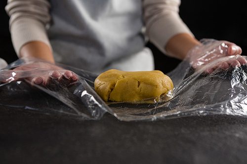 Mid section of woman wrapping dough in a plastic wrap