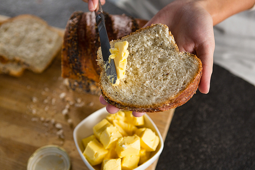 Close-up of woman applying butter over multigrain bread slice