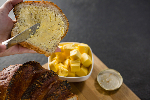 Close-up of woman applying butter over multigrain bread slice