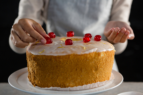 Mid section of woman toping a fresh baked cake with cherry