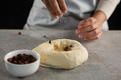 Mid section of woman adding chocolate chips into dough